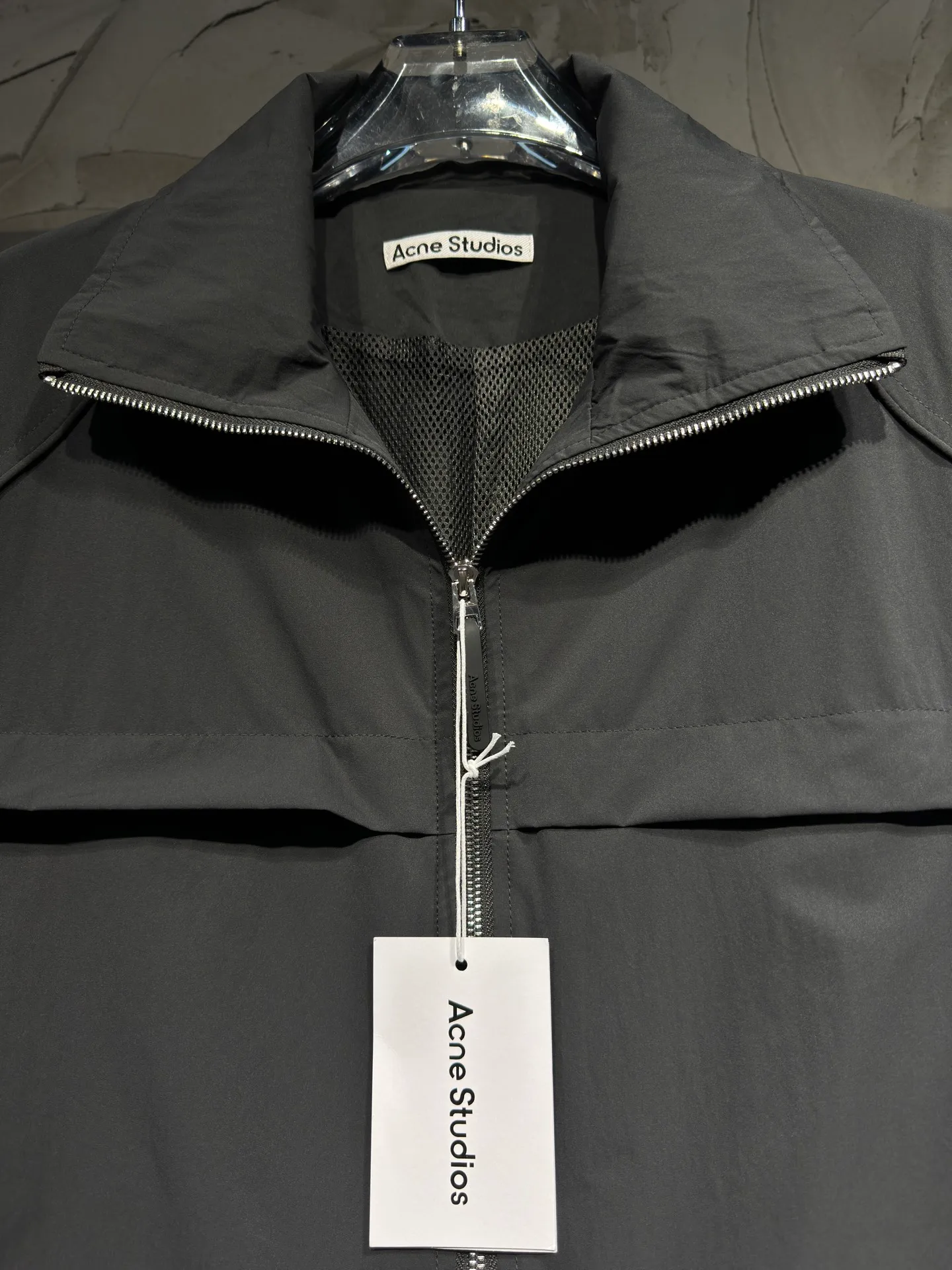 Acne Studios 26SS Large Lapel Short Jacket The fabric is made of 100% nylon (nylon/polyamide fiber) 75D high-density wrinkled nylon. The fabric has been permanently pressed and shaped by high temperature, and washed with high-pressure wrinkles at the factory to form its own irregular texture, permanently retaining the wrinkled texture, which will not disappear after washing. Matte matte coating removes the plastic glossy surface of nylon itself to create a low-key matte paper feel. Three-proof micro-coating, weak waterproof, anti-fouling, anti-static treatment, not easy to get dust. The interior is made of full-width mesh Breathable nylon lining, which reduces the stickiness of the nylon fabric to the body, improves air circulation, prevents sweating from sticking to the skin, and the zipper does not rub against the skin. The version adopts the raglan split topstitching process, and the front and rear panels are divided diagonally to expose even stitching. The three-dimensional dropped shoulders are loose and the fit is increased to increase the margin of movement. The back neckline is three-dimensional and high-density computer embroidered, and the embroidery lines are dense and not prickly. Customized all-metal matte nylon zipper, Genuine Leather embossed brand letters on the zipper leather tab, zipper tape with same color nylon fit to the body, double-locked reinforcement on both sides of the zipper to prevent pulling and tearing. Color: Gray Size: S M L